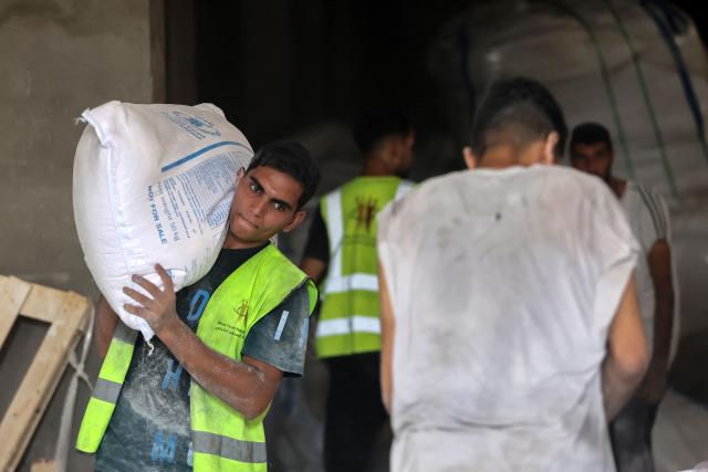 A Palestinian volunteer distributes bags of flower at a UN World Food Programme (WFP) warehouse on Al-Jalaa street in Gaza City, in the central Gaza Strip on July 12, 2025. Indirect talks between Hamas and Israel for a ceasefire in Gaza are being held up by Israel's proposals to keep troops in the territory, two Palestinian sources with knowledge of the discussions told AFP on July 12. (Photo by Omar AL-QATTAA / AFP)
