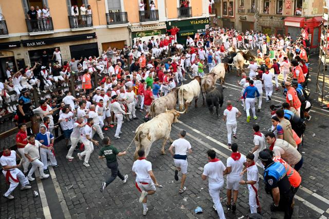 Participants run ahead of La Palmosilla breed bulls during the seventh running of the bulls of the San Fermin festival in Pamplona, northern Spain, on July 13, 2025. Thousands of people every year attend the week-long festival and its famous "encierros" or bull runs, every day at 8:00 a.m. through the narrow streets of the old town over an 850 meters (yard) course while runners ahead of them try to stay close to the bulls without falling over or being gored. (Photo by MIGUEL RIOPA / AFP)