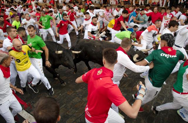 Participants run ahead of La Palmosilla breed bulls during the seventh running of the bulls of the San Fermin festival in Pamplona, northern Spain, on July 13, 2025. Thousands of people every year attend the week-long festival and its famous "encierros" or bull runs, every day at 8:00 a.m. through the narrow streets of the old town over an 850 meters (yard) course while runners ahead of them try to stay close to the bulls without falling over or being gored. (Photo by JORGE GUERRERO / AFP)