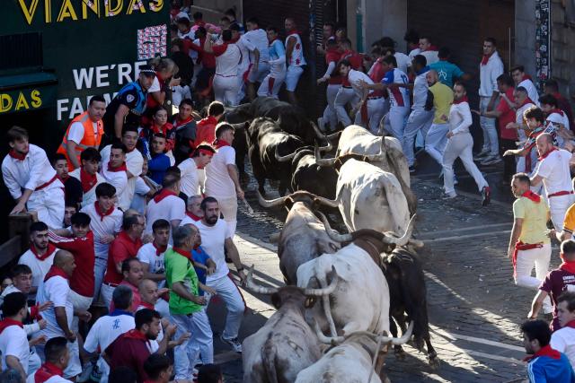 Participants run ahead of La Palmosilla breed bulls during the seventh running of the bulls of the San Fermin festival in Pamplona, northern Spain, on July 13, 2025. Thousands of people every year attend the week-long festival and its famous "encierros" or bull runs, every day at 8:00 a.m. through the narrow streets of the old town over an 850 meters (yard) course while runners ahead of them try to stay close to the bulls without falling over or being gored. (Photo by MIGUEL RIOPA / AFP)