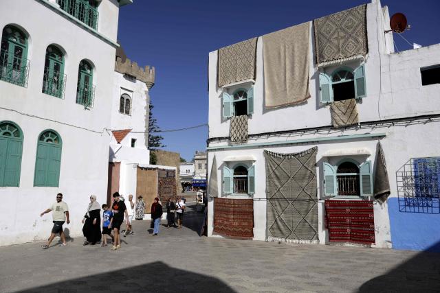 Visitors walk past a building covered in traditional tapestry during the annual Asilah Arts Festival, which transforms the coastal Moroccan town into an open air art gallery, on July 12, 2025. (Photo by Abdel Majid BZIOUAT / AFP)
