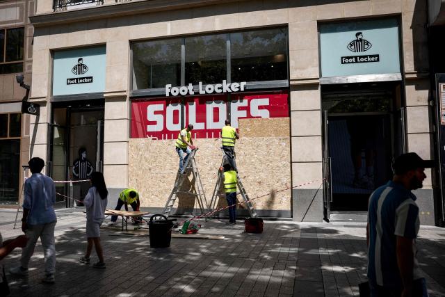 Workers cover the windows of a Foot Locker shop with OSB panels to protect against possible damage or looting that may be caused by people gathering during Bastille day celebrations or following a possible victory of the PSG football club in the FIFA Club World Cup final, on the Champs-Elysees Avenue in Paris on July 13, 2025. (Photo by Guillaume BAPTISTE / AFP)