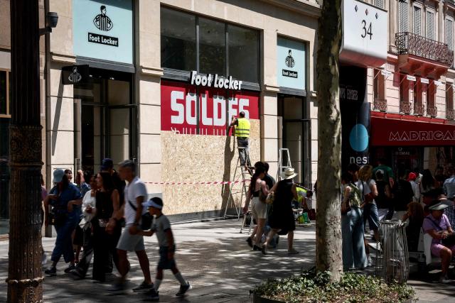 Workers cover the windows of a Foot Locker shop with OSB panels to protect against possible damage or looting that may be caused by people gathering during Bastille day celebrations or following a possible victory of the PSG football club in the FIFA Club World Cup final, on the Champs-Elysees Avenue in Paris on July 13, 2025. (Photo by Guillaume BAPTISTE / AFP)