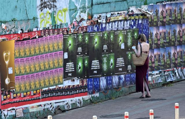 A woman enjoys a snack as she examines advertising placards in the centre of Kyiv on July 13, 2025. (Photo by Sergei SUPINSKY / AFP)