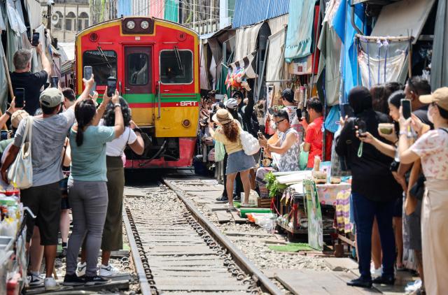 This photo taken on July 13, 2025 shows people taking photo of a passenger train passing through the Mae Klong railway market in Samut Songkhram province, around 80 kms (50 miles) southwest of Bangkok. (Photo by Sebastien BERGER / AFP)