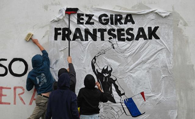 Young Basque independence supporters stick a banner on a wall reading "We are not French" during a demonstration against the celebration of July 14 in the Basque Country, called by the U14 collective (Uztailak 14-14 Juillet) in Espelette, southwestern France, on July 14, 2025. (Photo by Gaizka IROZ / AFP)