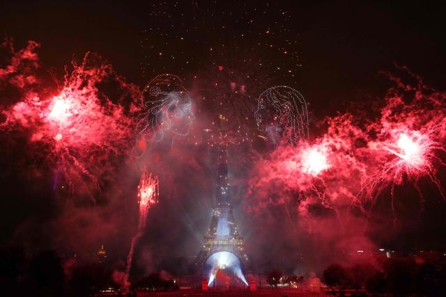 TOPSHOT - Fireworks explode around the Eiffel Tower as drones form two faces in profile during a choreographed light show to celebrate Bastille Day, in Paris, on July 14, 2025. (Photo by Dimitar DILKOFF / AFP)