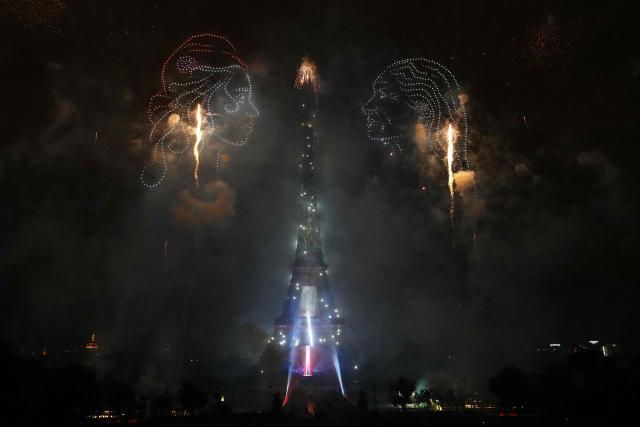 Drones create two faces in profile as fireworks light up around the Eiffel Tower during a choreographed light show to celebrate Bastille Day, in Paris, on July 14, 2025. (Photo by Dimitar DILKOFF / AFP)