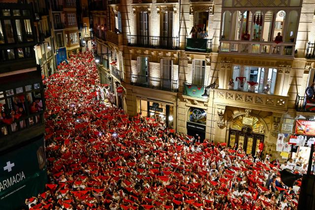 Revellers raise red scarves and candles as they sing the song "Pobre de Mi", marking the end of the San Fermin festival in Pamplona, Spain on July 14, 2025. Thousands of people attend the week-long festival and its famous "encierros" or bull runs. Every day at 8:00 a.m., bulls are released through the narrow streets of the old town over an 850-meter course while runners ahead of them try to stay close without falling over or being gored. (Photo by Ander GILLENEA / AFP)