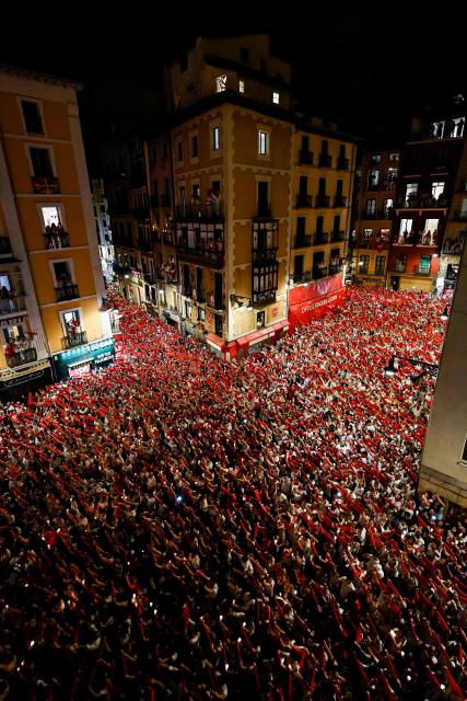 Revellers raise red scarves and candles as they sing the song "Pobre de Mi", marking the end of the San Fermin festival in Pamplona, Spain on July 14, 2025. Thousands of people attend the week-long festival and its famous "encierros" or bull runs. Every day at 8:00 a.m., bulls are released through the narrow streets of the old town over an 850-meter course while runners ahead of them try to stay close without falling over or being gored. (Photo by Ander GILLENEA / AFP)