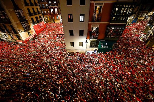 Revellers raise red scarves and candles as they sing the song "Pobre de Mi", marking the end of the San Fermin festival in Pamplona, Spain on July 14, 2025. Thousands of people attend the week-long festival and its famous "encierros" or bull runs. Every day at 8:00 a.m., bulls are released through the narrow streets of the old town over an 850-meter course while runners ahead of them try to stay close without falling over or being gored. (Photo by Ander GILLENEA / AFP)