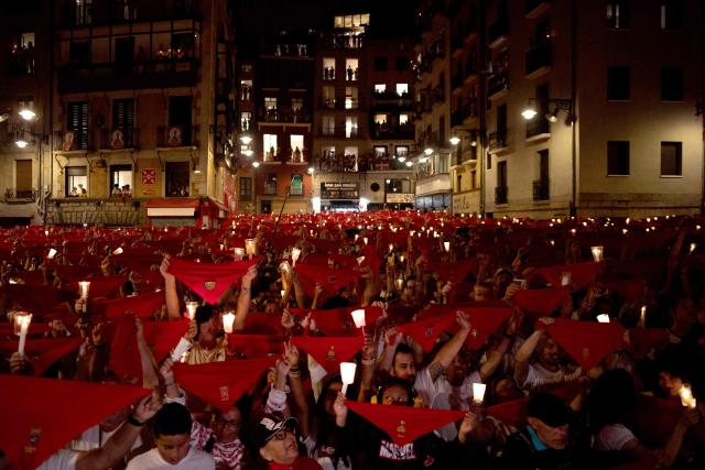 Revellers raise red scarves and candles as they sing the song "Pobre de Mi", marking the end of the San Fermin festival in Pamplona, Spain on July 14, 2025. Thousands of people attend the week-long festival and its famous "encierros" or bull runs. Every day at 8:00 a.m., bulls are released through the narrow streets of the old town over an 850-meter course while runners ahead of them try to stay close without falling over or being gored. (Photo by Jorge GUERRERO / AFP)