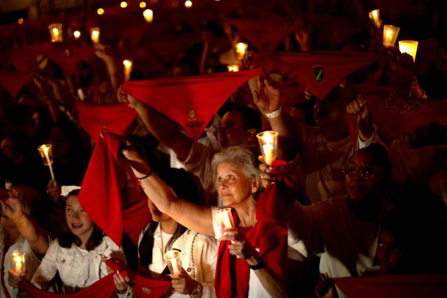 Revellers raise red scarves and candles as they sing the song "Pobre de Mi", marking the end of the San Fermin festival in Pamplona, Spain on July 14, 2025. Thousands of people attend the week-long festival and its famous "encierros" or bull runs. Every day at 8:00 a.m., bulls are released through the narrow streets of the old town over an 850-meter course while runners ahead of them try to stay close without falling over or being gored. (Photo by Jorge GUERRERO / AFP)