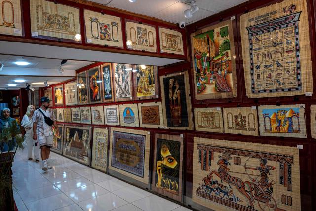 (FILES) Tourists visit a papyrus shop near the Great Pyramids plateau in Giza, south of Cairo, on June 10, 2025. The museum was expected to attract up to five million visitors annually, fuelling optimism across Cairo's battered tourism sector. But less than three weeks before its July 3 opening, the government announced another delay, this time pushing the landmark event to the final quarter of the year. (Photo by Khaled DESOUKI / AFP)