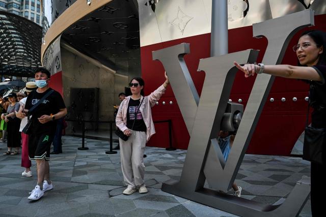 People pose for pictures next to "The Louis", a large ship-shaped structure of the Louis Vuitton brand, in Shanghai on June 15, 2025. (Photo by Hector RETAMAL / AFP)