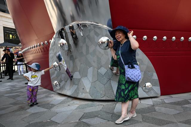 People pose for pictures next to "The Louis", a large ship-shaped structure of the Louis Vuitton brand, in Shanghai on June 15, 2025. (Photo by Hector RETAMAL / AFP)