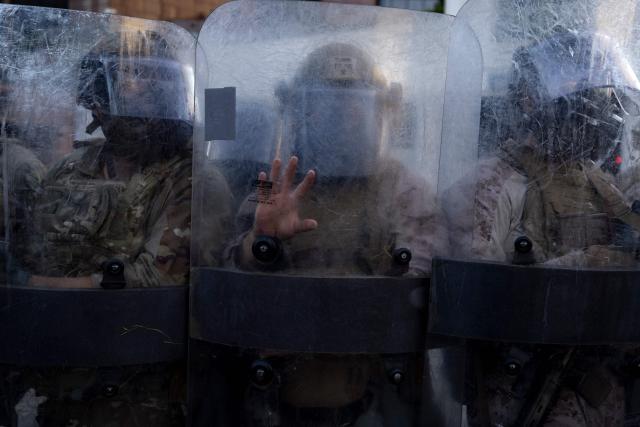 (FILES) US marines and members of the National Guard stand in a row protecting the entrance of the Metropolitan Detention Center as demonstrators gather in front of it following federal immigration operations, in Los Angeles, California on July 4, 2025. US Defense Secretary Pete Hegseth has ordered the withdrawal of 2,000 National Guard troops from Los Angeles, roughly halving the contentious deployment in the city, the Pentagon said on July 15, 2025. President Donald Trump ordered thousands of National Guard and hundreds of Marines into Los Angeles last month in response to protests over federal immigration sweeps -- a move opposed by city leaders and California's Democratic Governor Gavin Newsom. (Photo by Etienne LAURENT / AFP)