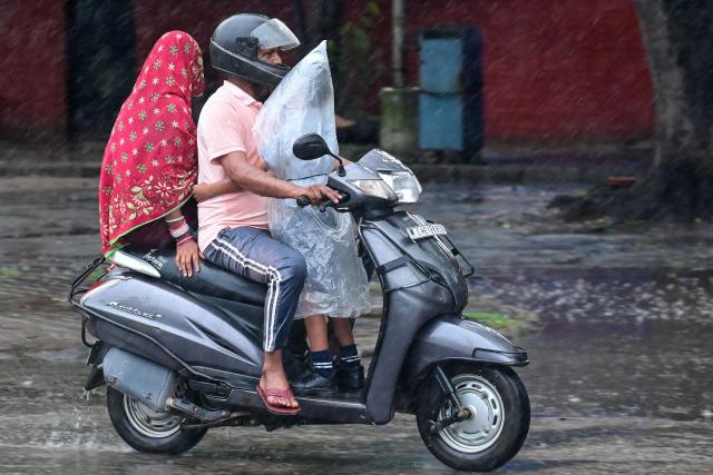 A schoolboy covered in a plastic sheet clings to an elder driving a scooter amid rainfall in Chandigarh on July 16, 2025. (Photo by AFP)