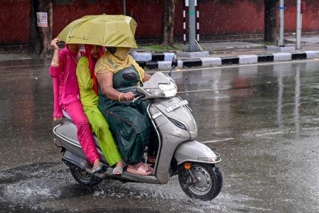TOPSHOT - Women ride a scooter while sharing an umbrella amid rainfall in Chandigarh on July 16, 2025. (Photo by AFP)