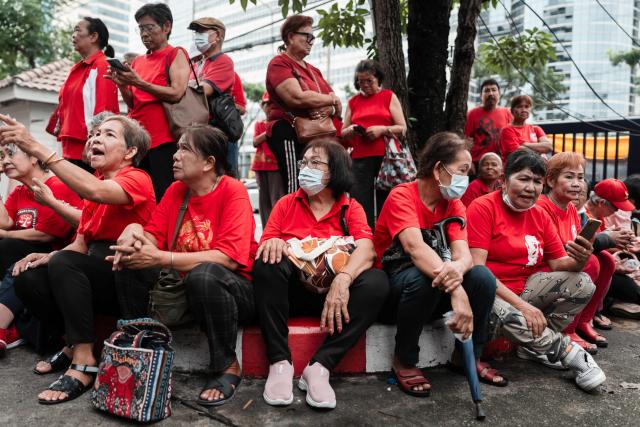 Supporters of Thailand's former prime minister Thaksin Shinawatra sit in front of the Criminal Court in Bangkok on July 16, 2025. Former Thai prime minister Thaksin Shinawatra is set to testify in court on July 16, seeking to defend himself against royal defamation charges in a watershed case for his faltering political dynasty. (Photo by Chanakarn Laosarakham / AFP)