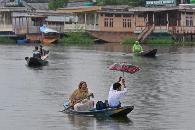A woman steers a boat as she ferries a child to school during a rainy morning on Dal Lake in Srinagar on July 16, 2025. (Photo by Tauseef MUSTAFA / AFP)