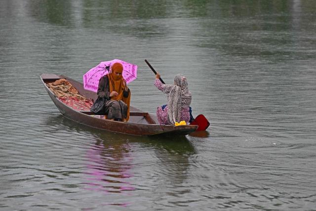 A woman steers a boat as a passenger holds an umbrella during a rainy morning on Dal Lake in Srinagar on July 16, 2025. (Photo by Tauseef MUSTAFA / AFP)
