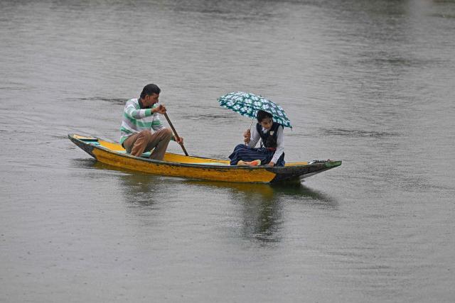 A man steers a boat as he ferries a child to school during a rainy morning on Dal Lake in Srinagar on July 16, 2025. (Photo by Tauseef MUSTAFA / AFP)