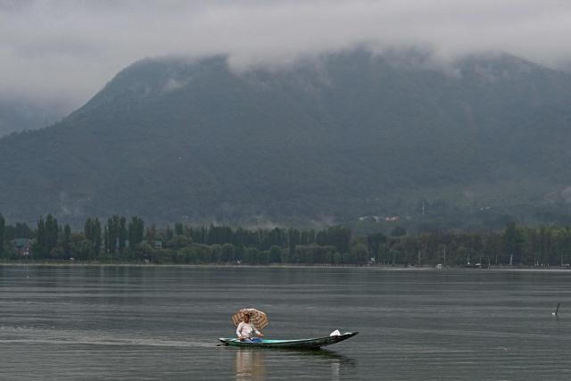 A man holds an umbrella as he steers a boat during a rainy morning on Dal Lake in Srinagar on July 16, 2025. (Photo by Tauseef MUSTAFA / AFP)