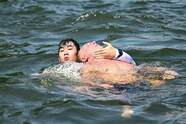 France's swimmer Marc-Antoine Olivier (R) is pulled out from the water in the final of the men's 10km open water swimming event during the 2025 World Aquatics Championships at Sentosa Island in Singapore on July 16, 2025. (Photo by Manan VATSYAYANA / AFP)