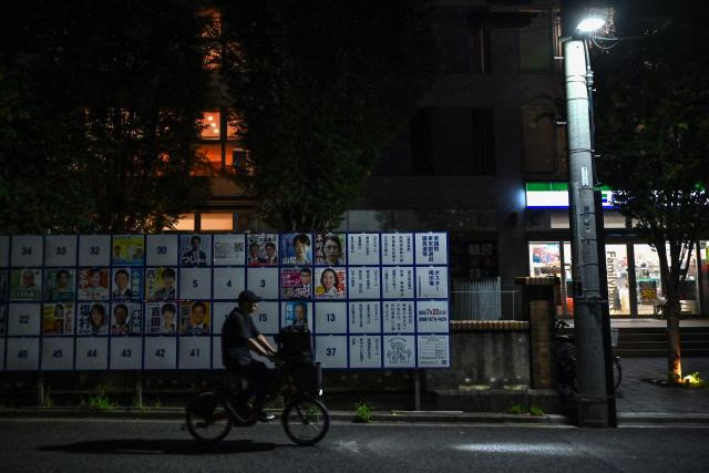 A man cycles past an election poster bulletin board showing different candidates in the upcoming July 20 upper house election, in central Tokyo on July 16, 2025. Japan's unpopular ruling coalition faces tough upper house elections on July 20, opinion polls suggested, potentially ending Shigeru Ishiba's premiership after less than a year. (Photo by Richard A. Brooks / AFP)