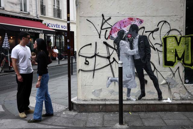 A couple stand near a street art graffiti in Paris on July 18, 2025. (Photo by Behrouz MEHRI / AFP)