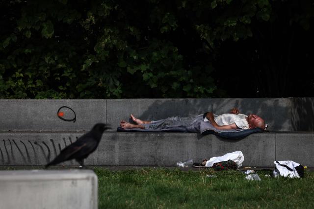 A craw sits near a man sleeping on a bench in Chatelet district in Paris on July 18, 2025. (Photo by Behrouz MEHRI / AFP)
