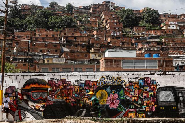 A downhill rider participates in the Petare en Alta urban downhill competition in front of a mural in Petare, Miranda state, Venezuela on July 18, 2025. (Photo by Pedro MATTEY / AFP)