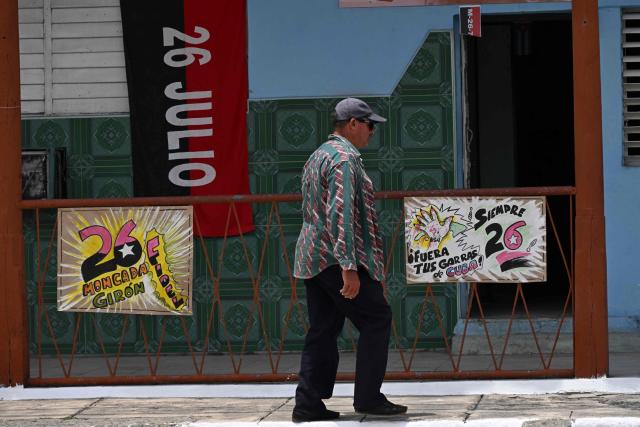 A man walks past a 26th of July Movement flag in tribute to the 72nd anniversary of the assault on the Moncada Barracks in 1953, in Jatibonico, Sancti Spiritus province, Cuba on July 23, 2025. The Cuban government on July 26 will commemorate the 72nd anniversary of the guerrilla assault on the Moncada Barracks, widely regarded as the beginning of the Cuban Revolution. (Photo by YAMIL LAGE / AFP)