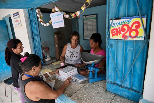 Cubans buy groceries at a store with a sign that reads in spanish 'We are on 26,' in tribute to the 72nd anniversary of the assault on the Moncada Barracks in 1953, in Ciego de Avila province, Cuba on July 23, 2025. The Cuban government on July 26 will commemorate the 72nd anniversary of the guerrilla assault on the Moncada Barracks, widely regarded as the beginning of the Cuban Revolution. (Photo by YAMIL LAGE / AFP)