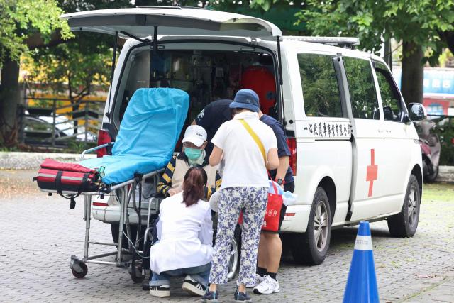 A voter receives assistance on a wheelchair after arriving at a polling station by ambulance to vote in the recall election in Taipei on July 26, 2025. Taiwanese voters turned out at schools, churches and community centres on July 26 to cast their ballot in a high-stakes recall election that could give President Lai Ching-te's party control of the parliament. (Photo by I-Hwa Cheng / AFP)
