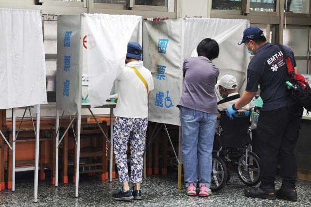 A voter on a wheelchair (2nd R) is brought to a booth after arriving at a polling station by ambulance to vote in the recall election in Taipei on July 26, 2025. Taiwanese voters turned out at schools, churches and community centres on July 26 to cast their ballot in a high-stakes recall election that could give President Lai Ching-te's party control of the parliament. (Photo by I-Hwa Cheng / AFP)