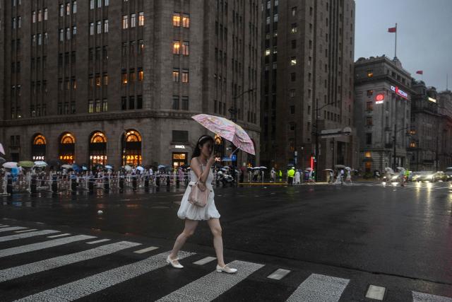 A woman uses an umbrella during the passage of Typhoon Co-May on The Bund, in Shanghai on July 30, 2025. Shanghai has evacuated almost 283,000 people from vulnerable coastal and low-lying areas as Typhoon Co-May approaches, bringing lashing rains and high winds, state media reported on July 30. (Photo by Hector RETAMAL / AFP)