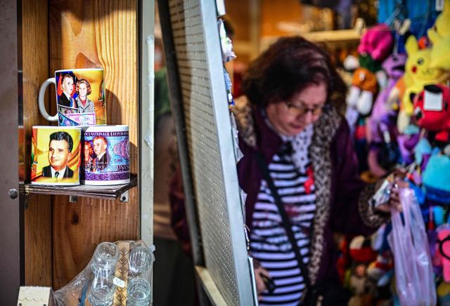 A woman leaves souvenir shop displays mugs with the portraits of late communist dictator Nicolae Ceausescu, his wife Elena and communist-erac banknotes in Baile Herculane, south-western Romania on July 29, 2025. A recent survey shows a worring nostalgic trend such as 55.8% of Romanians believe that the communist regime was rather a good thing for Romania, 48.4% think that life was better before 1989 compared to today, 77.2% believe that Romania was a richer country before 1989, 75.1% believe movies produced in Romania before 1989 were better than today.  President Nicusor Dan's reacts with a tweet about the survey: "I am deeply concerned about the results of the study presented today". "In my opinion, the main reason why more and more Romanians are idealizing communism is the deep disappointment with the political class of the last three decades." (Photo by Daniel MIHAILESCU / AFP)
