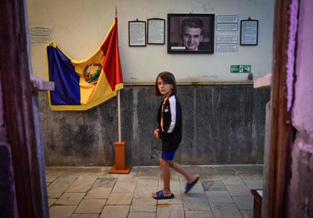 TOPSHOT - A child walk past a portrait of late communist dictator Nicolae Ceausescu and a flag of socialist Romania displayed for visitors at "Apollo Baths" - a private museum in Baile Herculane, south-western Romania on July 29, 2025. A recent survey shows a worring nostalgic trend such as 55.8% of Romanians believe that the communist regime was rather a good thing for Romania, 48.4% think that life was better before 1989 compared to today, 77.2% believe that Romania was a richer country before 1989, 75.1% believe movies produced in Romania before 1989 were better than today.  President Nicusor Dan's reacts with a tweet about the survey: "I am deeply concerned about the results of the study presented today". "In my opinion, the main reason why more and more Romanians are idealizing communism is the deep disappointment with the political class of the last three decades." (Photo by Daniel MIHAILESCU / AFP)
