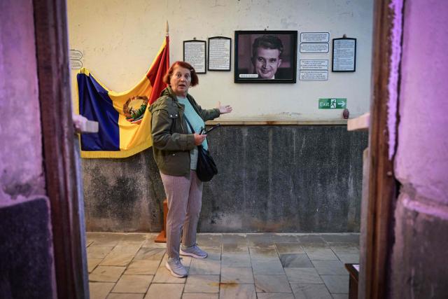 A woman gestures as she walks past a portrait of late communist dictator Nicolae Ceausescu and a flag of socialist Romania displayed for visitors at "Apollo Baths" - a private museum in Baile Herculane, south-western Romania on July 29, 2025. A recent survey shows a worring nostalgic trend such as 55.8% of Romanians believe that the communist regime was rather a good thing for Romania, 48.4% think that life was better before 1989 compared to today, 77.2% believe that Romania was a richer country before 1989, 75.1% believe movies produced in Romania before 1989 were better than today.  President Nicusor Dan's reacts with a tweet about the survey: "I am deeply concerned about the results of the study presented today". "In my opinion, the main reason why more and more Romanians are idealizing communism is the deep disappointment with the political class of the last three decades." (Photo by Daniel MIHAILESCU / AFP)