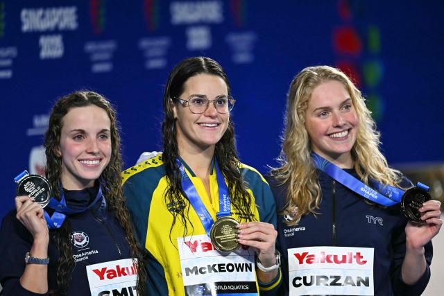 (L-R) Silver medallist US' swimmer Regan Smith, gold medallist Australia's swimmer Kaylee McKeown and bronze medallist US' swimmer Claire Curzan celebrate on the podium the women's 200m backstroke swimming event during the 2025 World Aquatics Championships in Singapore on August 2, 2025. (Photo by MANAN VATSYAYANA / AFP)