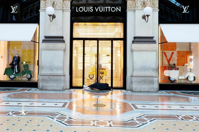 A person sleeps in the doorway of Luis Vuitton flagship store in Vittorio Emanuele II gallery, central Milan, on August 5, 2025. (Photo by Stefano RELLANDINI / AFP)