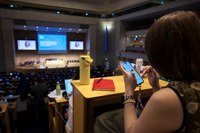 A woman uses her mobile phone at the media tribune of the assembly hall at the start of plastics treaty negotiations at the United Nations Offices in Geneva on August 5, 2025. Countries were to start the clock on August 5, 2025 on 10 days of talks aimed at hammering out a landmark global treaty on combating the scourge of plastic pollution. Three years of negotiations hit the wall in South Korea in December 2024 when a group of oil-producing states blocked a consensus. (Photo by Fabrice COFFRINI / AFP)