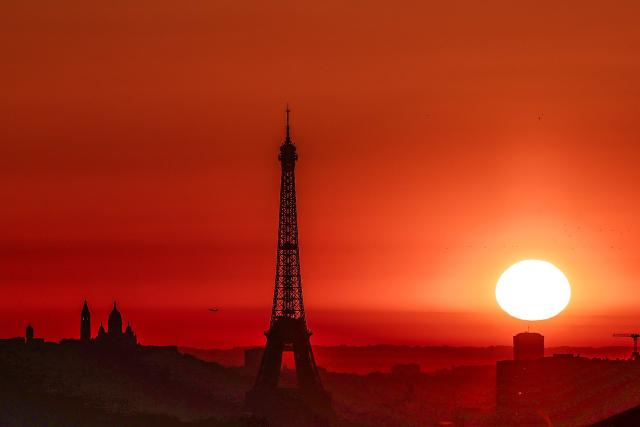 (FILES) The sun rises by the Eiffel Tower and the Sacre Coeur Basilica ontop of the Montmartre hill in Paris on July 1, 2025, as the city is on red alert for high temperatures, with the top of the Eiffel Tower shut, polluting traffic banned and speed restrictions in place as a searing heatwave gripped Europe. Some resist, others crack: Paris does not have a culture of individual air conditioning, but with the intensification of heat waves, the issue is becoming increasingly pressing and poses a dilemma for those who are aware of the damage it causes.‘It was up to 41 degrees in my home during the last heatwave. I didn't think that was possible,’ sighs Marion Laruste, who lives in an attic in the north-east of the capital. (Photo by Thibaud MORITZ / AFP)