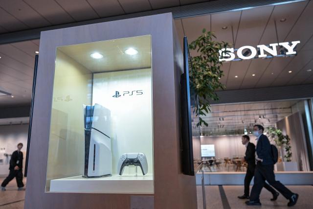 (FILES) This file photo taken on November 27, 2024 shows people walking past a display case (L) showing a new PlayStation 5, in the lobby of the Sony headquarters building in central Tokyo. Japan's Sony raised its net profit forecast for the current financial year to 970 billion yen (6.6 billion USD) on August 7, 2025, up from the previous estimate of 930 billion yen. (Photo by Richard A. Brooks / AFP)