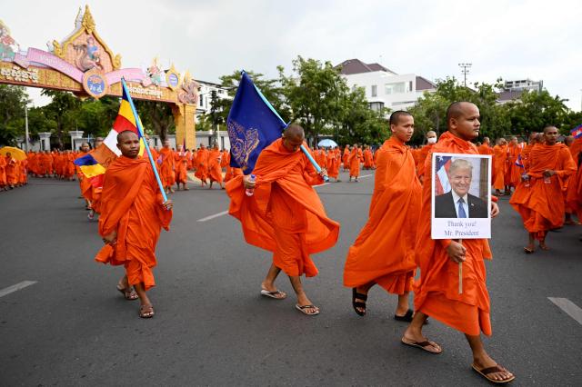 A Cambodian Buddhist monk (R) holds a placard showing a portrait of US President Donald Trump as he takes part in a march for peace in Phnom Penh on August 10, 2025, following a border conflict with Thailand. (Photo by TANG CHHIN Sothy / AFP)