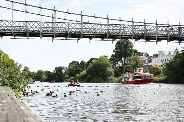 People on a pedalo enjoy the fine weather as a river cruiser passes, on the River Dee in Chester, north west England on August 11, 2025. Amber heat health warnings have been issued across many areas of England, as temperatures are expected to reach the mid-30s. (Photo by Paul ELLIS / AFP)