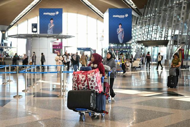 Passengers use trolleys to carry their luggage at Kuala Lumpur International Airport in Sepang on August 12, 2025. (Photo by Mohd RASFAN / AFP)