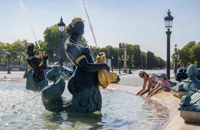 (FILES) A woman and a child cool their hands in the Fontaine des Mers fountain spraying water at the Place de la Concorde in Paris on August 11, 2025, amid a heatwave in Europe. The red heat alert remains in force until August 13 in the 14 departments of the South-West and the Centre-East concerned, Meteo-France announced in its latest bulletin, on August 12, 2025. (Photo by Martin LELIEVRE / AFP)